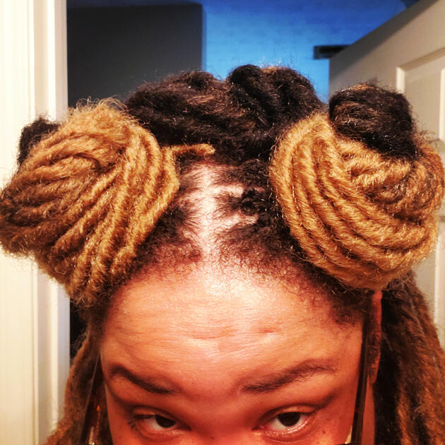 A black trans hottie with two buns of faux locs